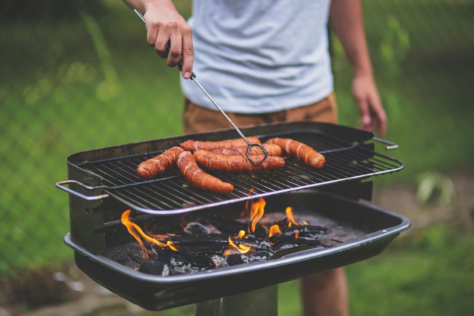 A person uses tongs to move a sausage on a charcoal barbecue